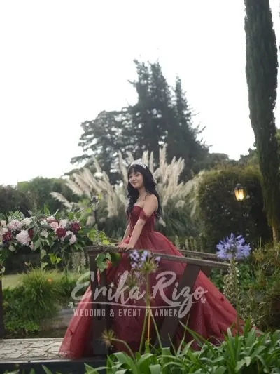 Quinceañera sobre un puente de madera entre jardines
